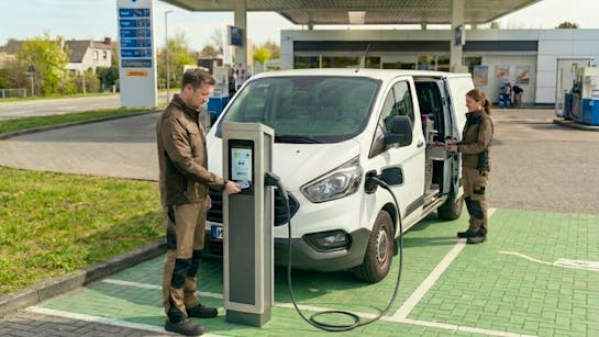 Personen laden Transportauto an einer Tankstelle und bezahlen mit Ladekarte