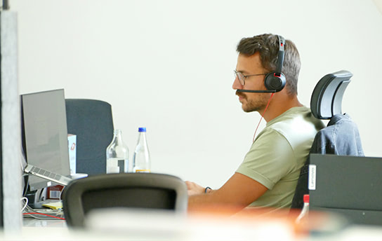 Fokus Mitarbeiter sitzt an seinem Arbietsplatz und trägt ein Headset